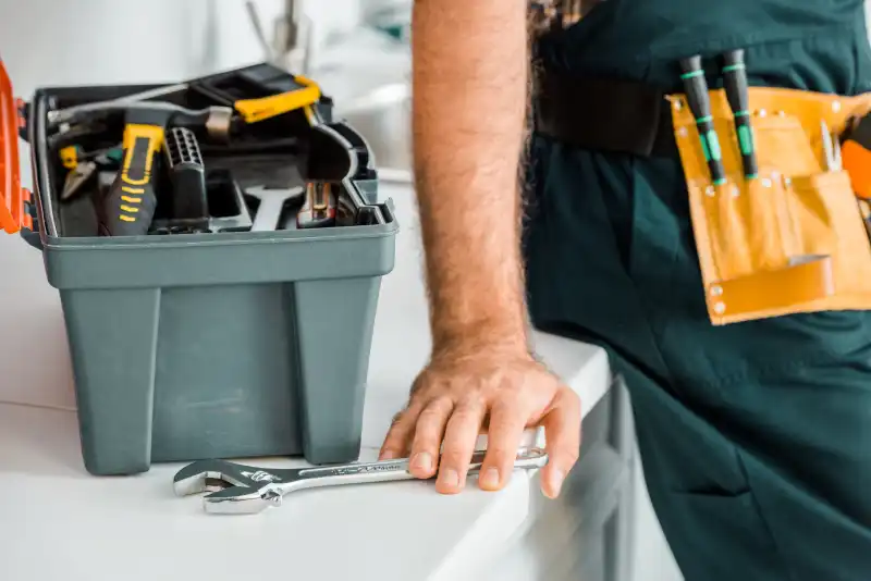 No Installation Fees cropped image of plumber leaning on kitchen counter and touching adjustable wrench in kitchen